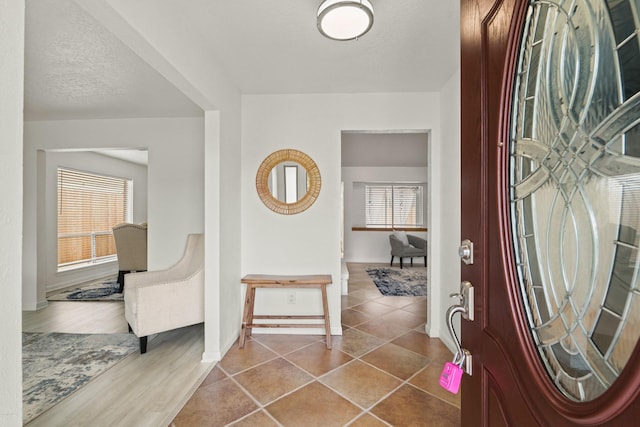 foyer entrance featuring a textured ceiling, tile patterned floors, and a healthy amount of sunlight