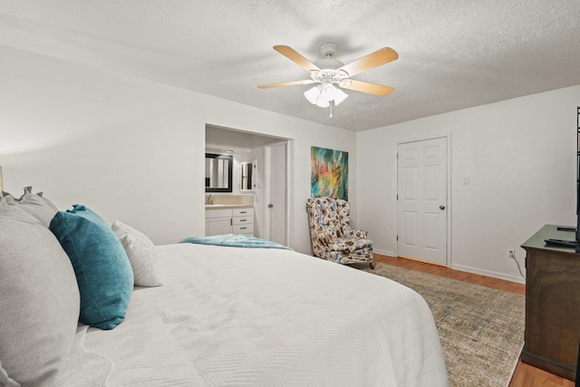 bedroom with sink, ensuite bath, a textured ceiling, light hardwood / wood-style floors, and ceiling fan