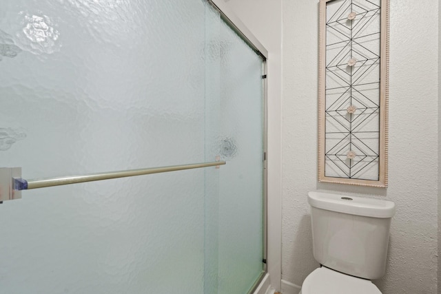 bathroom featuring a shower with shower door and toilet