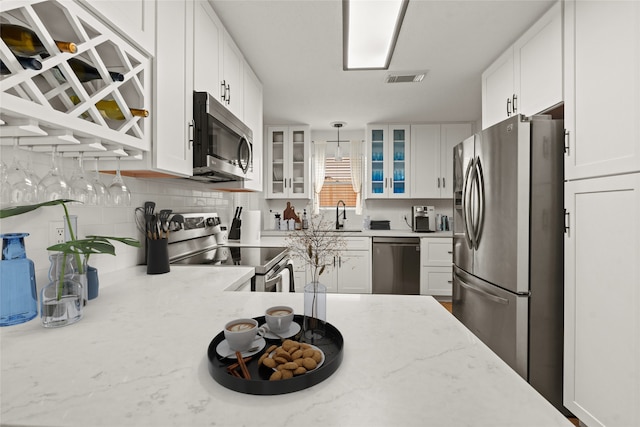 kitchen with appliances with stainless steel finishes, tasteful backsplash, light stone countertops, white cabinets, and decorative light fixtures