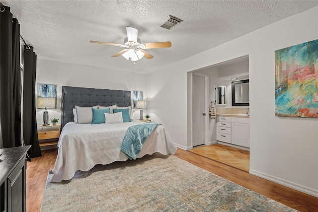 bedroom featuring light wood-type flooring, a textured ceiling, ceiling fan, and ensuite bath