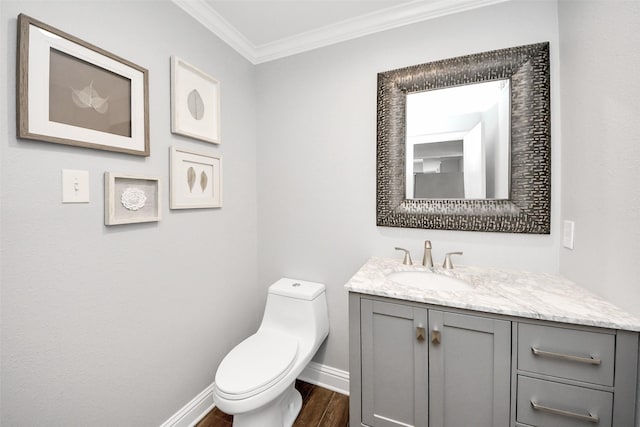 bathroom with crown molding, toilet, vanity, wood finished floors, and baseboards