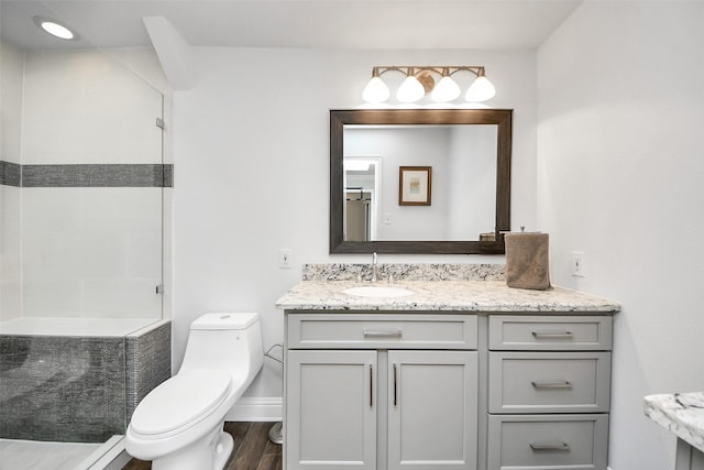 bathroom with tiled shower, vanity, toilet, and wood finished floors