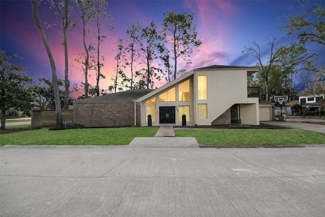 mid-century home featuring a balcony, a garage, brick siding, driveway, and a lawn