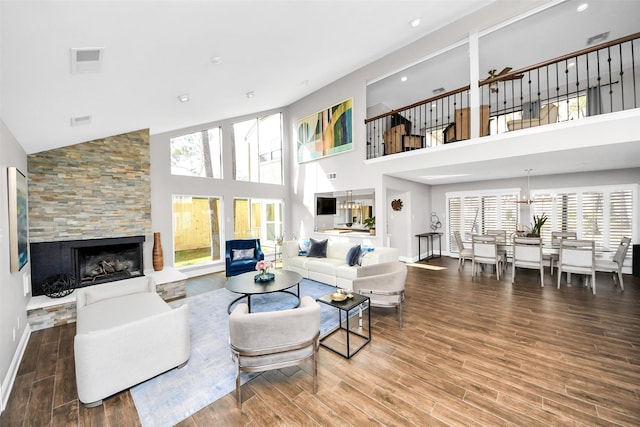 living room with baseboards, visible vents, wood finished floors, a fireplace, and high vaulted ceiling