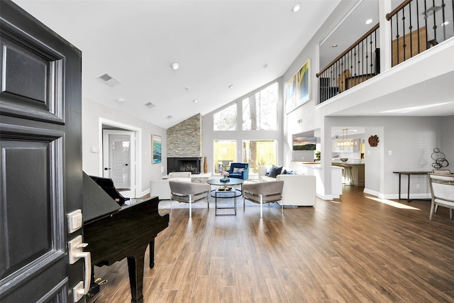 living room featuring a fireplace, visible vents, a towering ceiling, wood finished floors, and baseboards