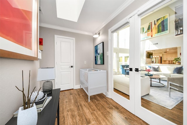 entryway with a skylight, crown molding, visible vents, wood finished floors, and baseboards