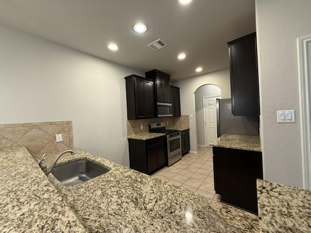 kitchen featuring appliances with stainless steel finishes, sink, light stone counters, light tile patterned flooring, and decorative backsplash