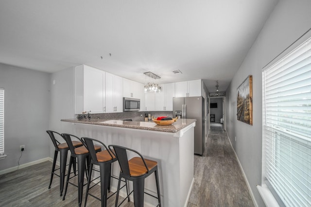 kitchen featuring kitchen peninsula, light stone countertops, appliances with stainless steel finishes, white cabinets, and a kitchen bar