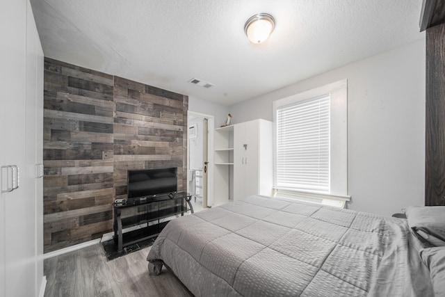 bedroom with hardwood / wood-style flooring, wood walls, and a textured ceiling