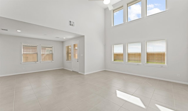 unfurnished living room with a high ceiling, light tile patterned flooring, visible vents, and baseboards