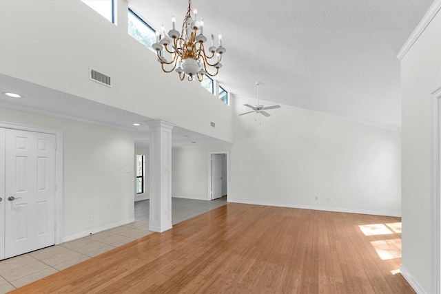 unfurnished living room featuring ornate columns, healthy amount of natural light, a ceiling fan, a chandelier, and a high ceiling