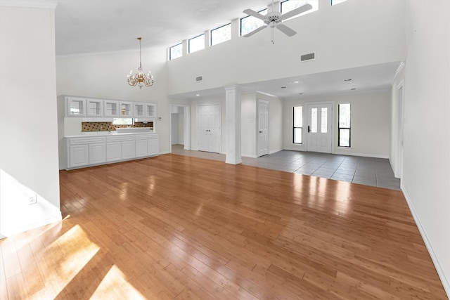 unfurnished living room with a high ceiling, a ceiling fan, baseboards, a chandelier, and light wood finished floors