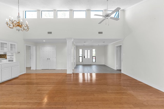 unfurnished living room featuring decorative columns, light hardwood / wood-style floors, a high ceiling, ornamental molding, and ceiling fan with notable chandelier