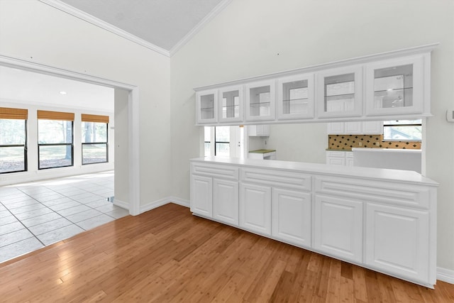 empty room featuring ornamental molding, lofted ceiling, light wood-style flooring, and baseboards
