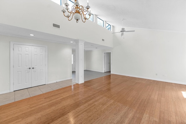 unfurnished living room featuring ceiling fan with notable chandelier, light wood-type flooring, decorative columns, and a high ceiling