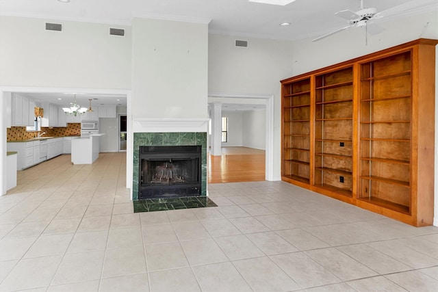 unfurnished living room with light tile patterned floors, a tiled fireplace, ceiling fan, ornamental molding, and sink