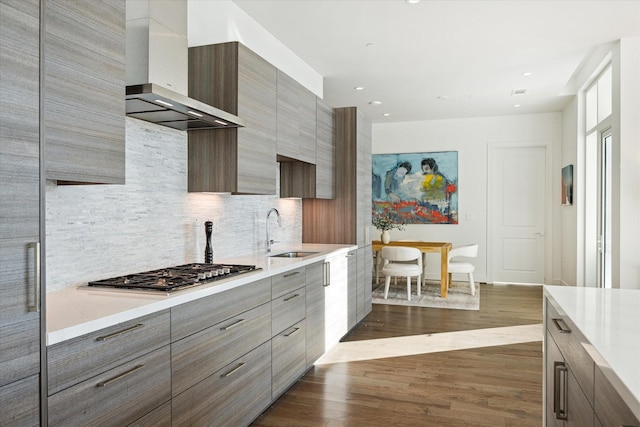 kitchen with sink, dark wood-type flooring, wall chimney exhaust hood, stainless steel gas cooktop, and decorative backsplash