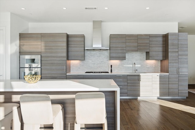 kitchen with sink, backsplash, wall chimney range hood, a kitchen bar, and dark hardwood / wood-style floors