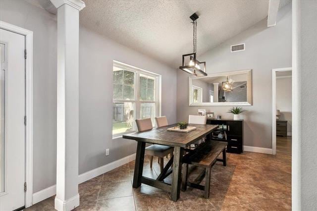 dining room featuring decorative columns, vaulted ceiling, and a textured ceiling