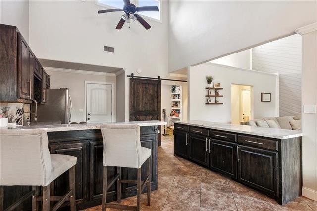 interior space with a barn door, a kitchen island, stainless steel refrigerator, ceiling fan, and a kitchen bar