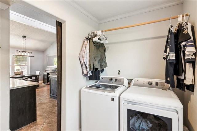 clothes washing area featuring light tile patterned floors, ornamental molding, and washing machine and clothes dryer