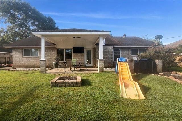 rear view of house with an outdoor fire pit, a lawn, a patio area, a playground, and ceiling fan