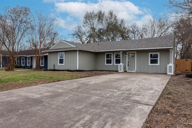 ranch-style home with a shingled roof, a front yard, and fence