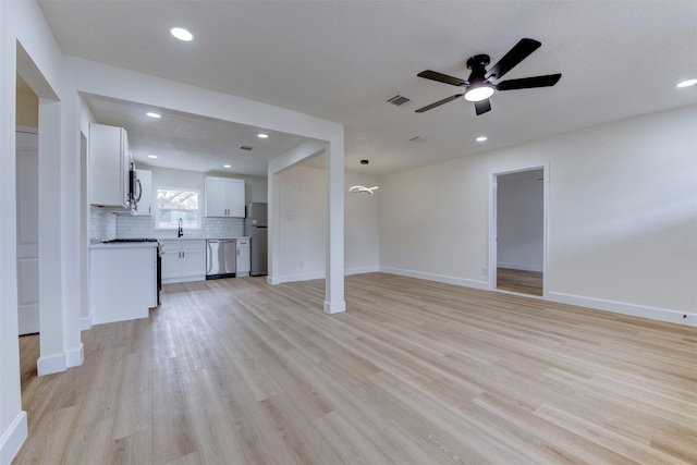 unfurnished living room with light wood-type flooring, sink, and ceiling fan