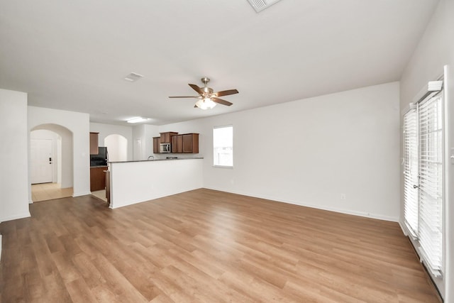 unfurnished living room featuring light wood-style floors, arched walkways, visible vents, and a ceiling fan