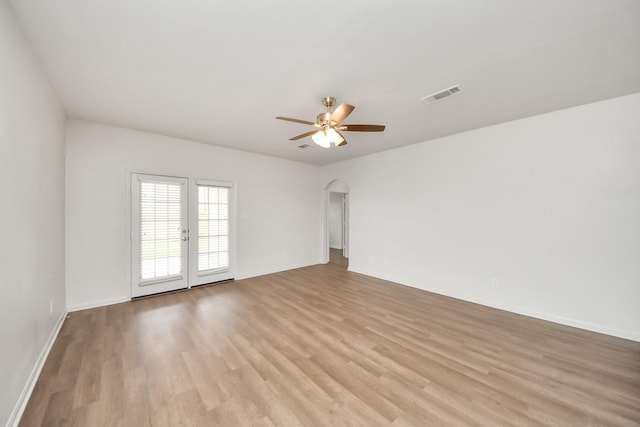 empty room featuring arched walkways, visible vents, light wood-style floors, a ceiling fan, and baseboards