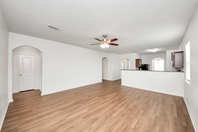 unfurnished living room featuring light wood finished floors, visible vents, arched walkways, and a ceiling fan