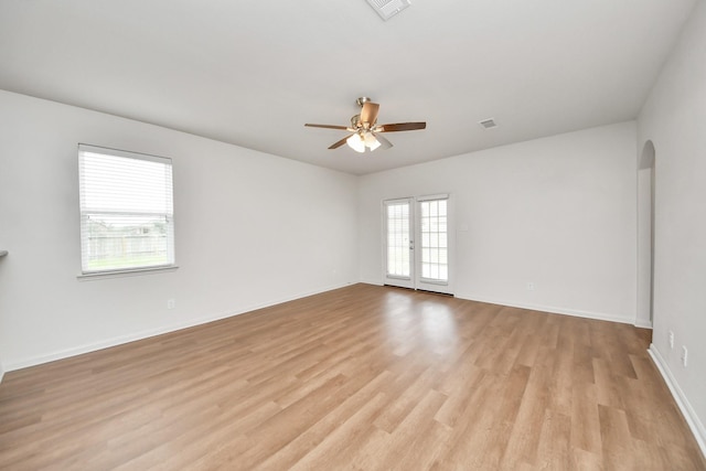 unfurnished room featuring arched walkways, light wood-type flooring, a ceiling fan, and baseboards