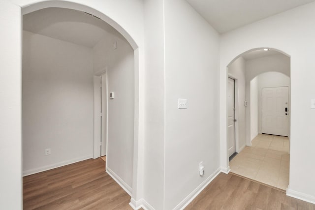 hall featuring light wood-type flooring, arched walkways, and baseboards