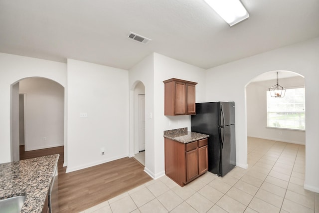 kitchen with brown cabinets, visible vents, freestanding refrigerator, light tile patterned flooring, and dark stone countertops