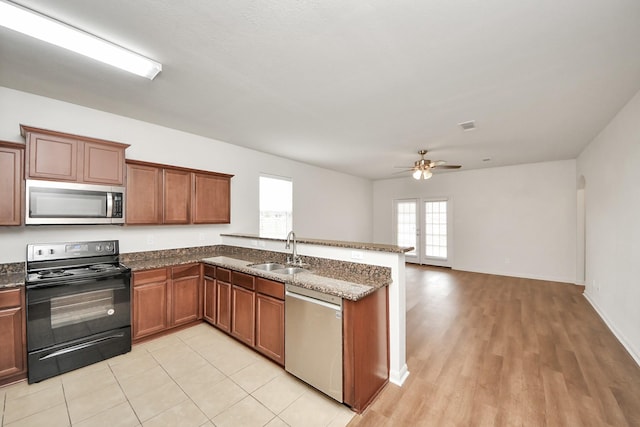 kitchen with brown cabinets, appliances with stainless steel finishes, open floor plan, a sink, and dark stone counters