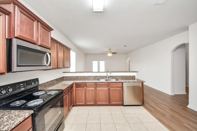 kitchen with arched walkways, stainless steel appliances, brown cabinetry, a sink, and a peninsula