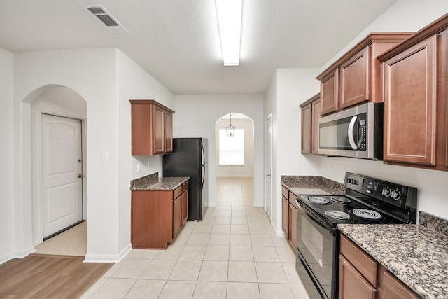 kitchen with arched walkways, brown cabinets, visible vents, dark stone countertops, and black appliances