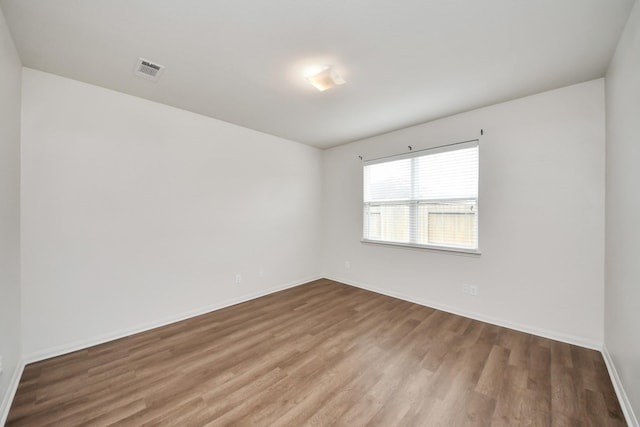 empty room featuring wood finished floors, visible vents, and baseboards