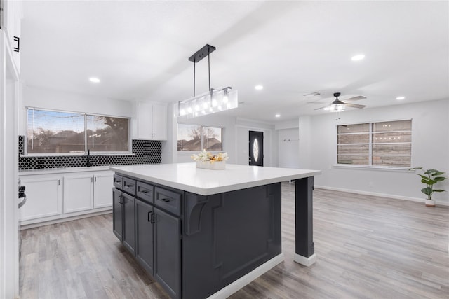 kitchen with light wood-type flooring, white cabinetry, a kitchen island, hanging light fixtures, and a breakfast bar area