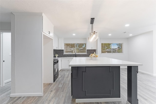 kitchen with backsplash, stove, a kitchen island, white cabinets, and hanging light fixtures