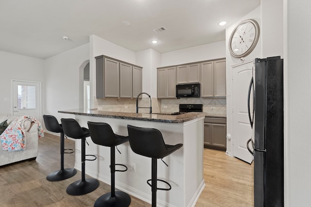 kitchen featuring gray cabinets, dark stone counters, a kitchen bar, and black appliances