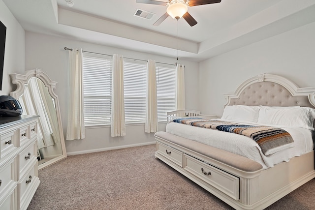 carpeted bedroom with a raised ceiling, multiple windows, and ceiling fan