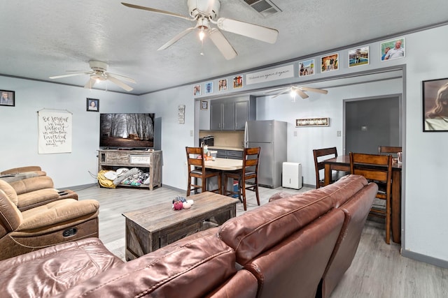 living room with ceiling fan, light hardwood / wood-style flooring, and a textured ceiling