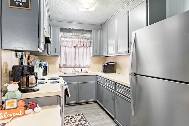 kitchen with sink, gray cabinets, a textured ceiling, light hardwood / wood-style floors, and stainless steel refrigerator