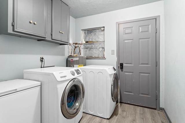 laundry area featuring electric water heater, independent washer and dryer, cabinets, and light hardwood / wood-style floors