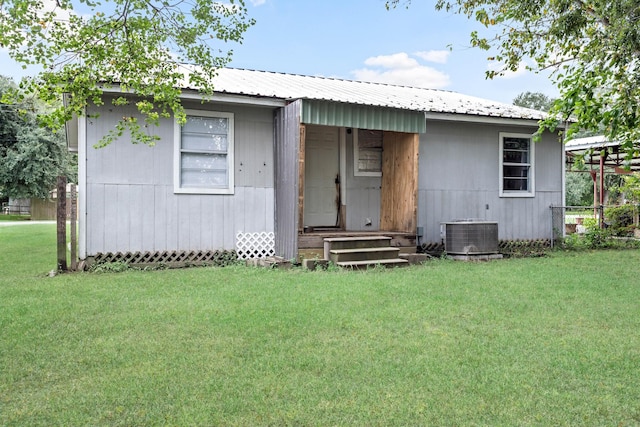 rear view of property featuring central air condition unit and a lawn