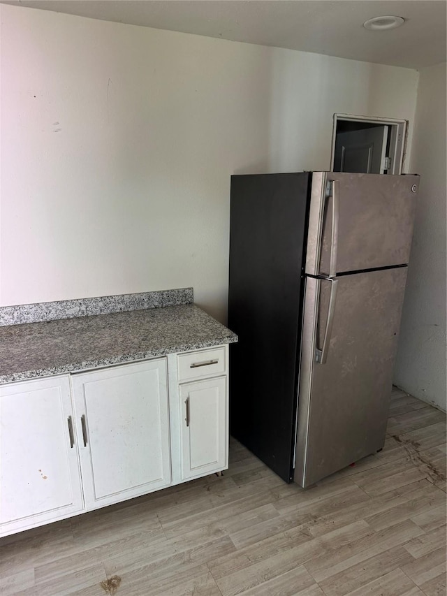 kitchen with white cabinets, light wood-type flooring, light stone countertops, and stainless steel fridge