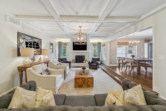 living room with beam ceiling, wood-type flooring, a chandelier, coffered ceiling, and a brick fireplace