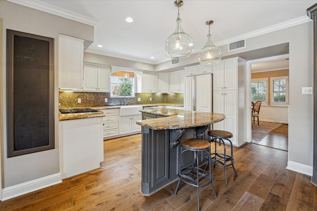 kitchen with a kitchen island, white cabinetry, paneled built in fridge, and light stone counters